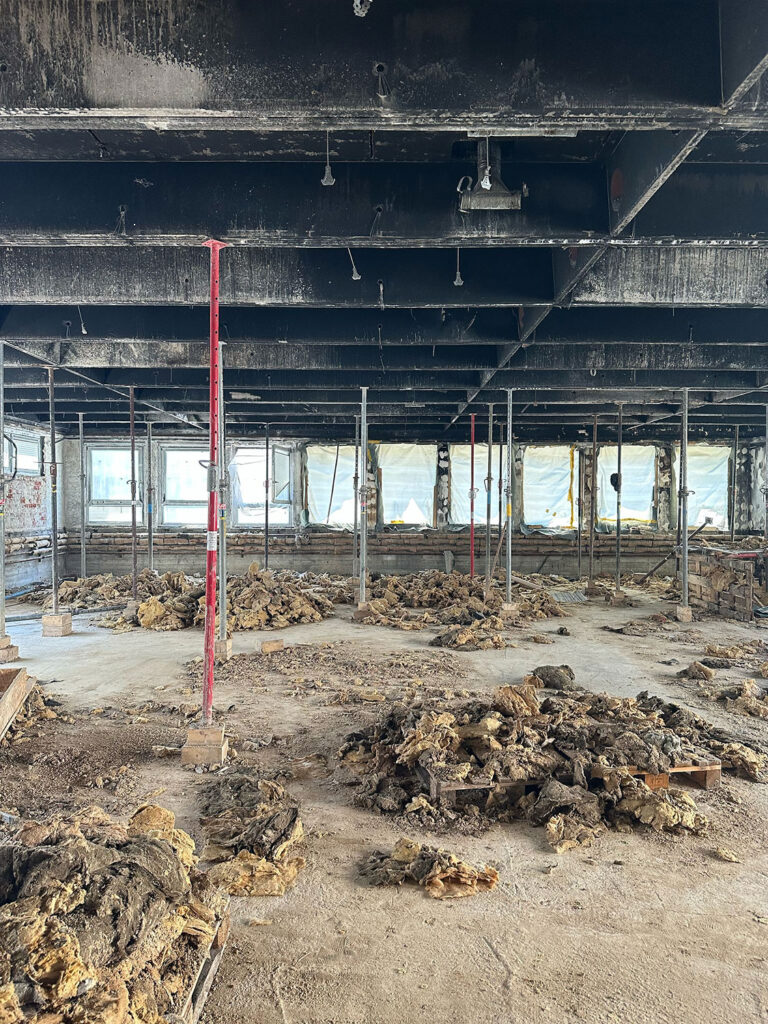 Gutachten - Raum nach Brandschaden mit vielen Baustützen auf dem Boden liegt haufenweise alte verruste Dämmwolle